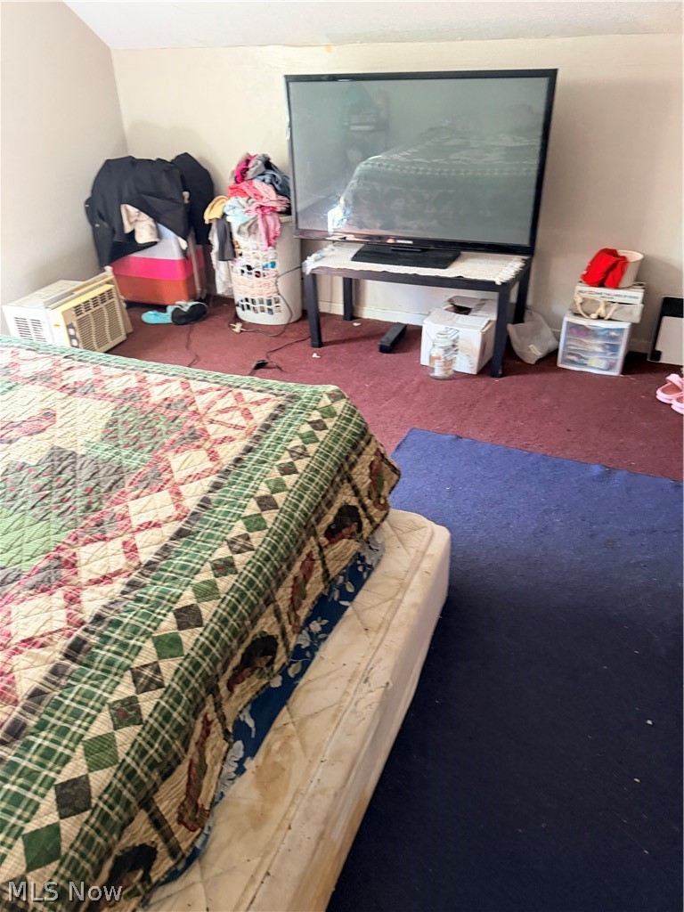 Bedroom with a patterned quilt-covered bed, large television, and window air conditioner.
