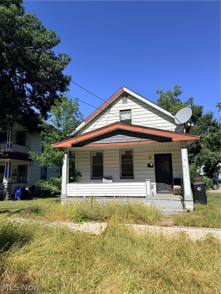 Two-story house with a red-trimmed porch roof and overgrown front yard.