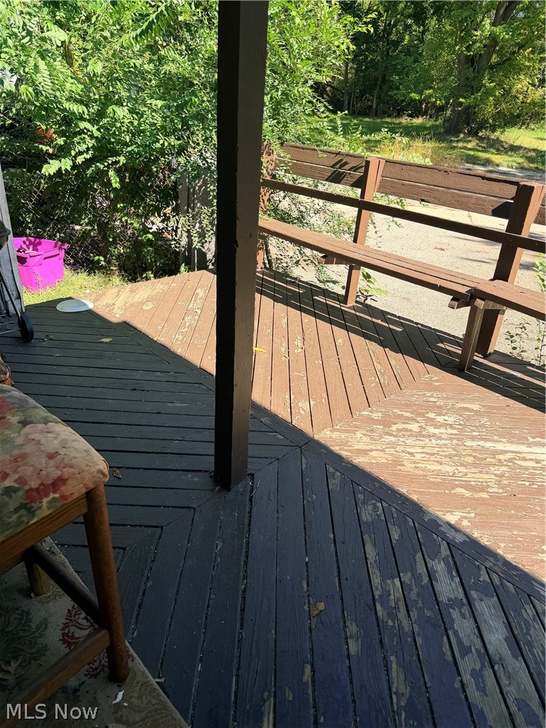 Wooden porch deck with a brown railing and dense greenery beyond.