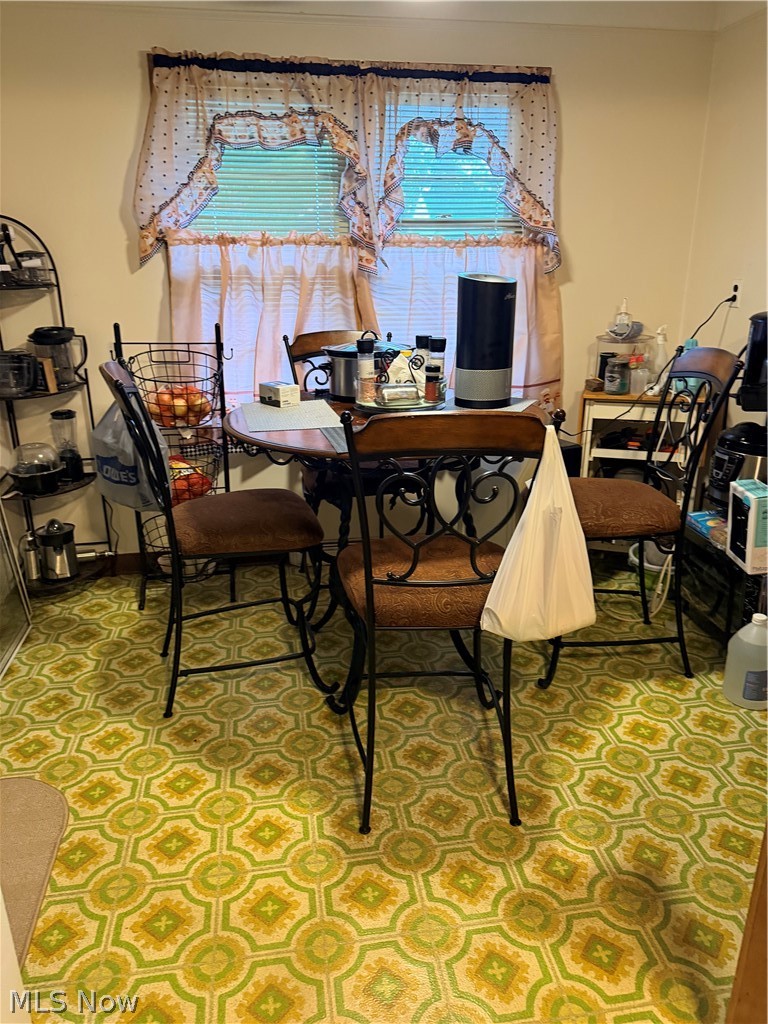 Dining area with a small table, ornate metal chairs, curtained windows, and a patterned green-and-yellow floor.
