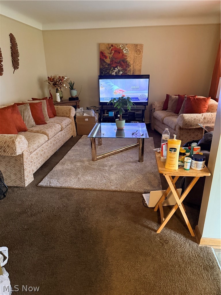 Furnished living room with patterned sofas, rust-colored pillows, and a glass coffee table.