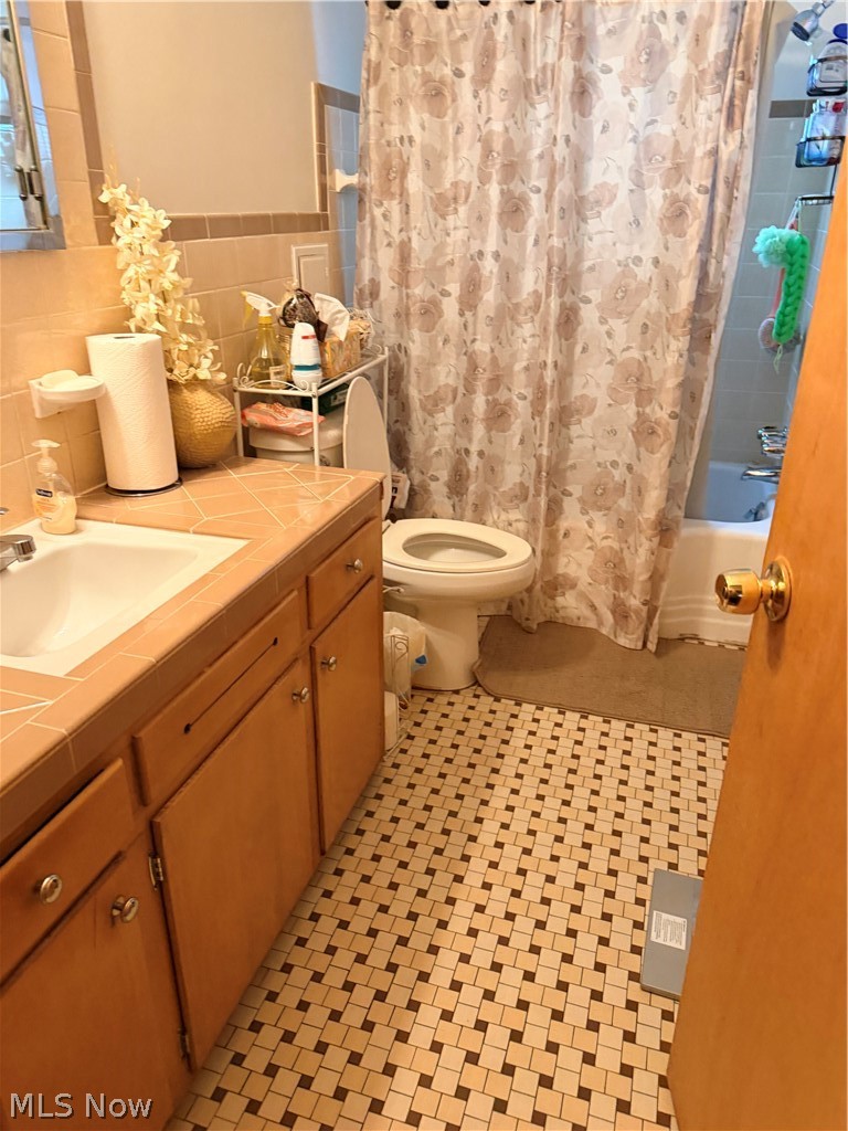 Bathroom with a wood vanity, patterned shower curtain, and mosaic tile floor.