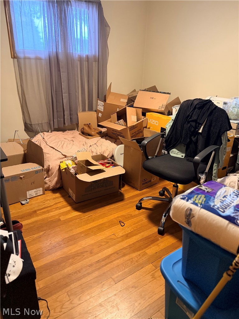 Bedroom with hardwood floors, a bed, office chair, and boxes packed with belongings.