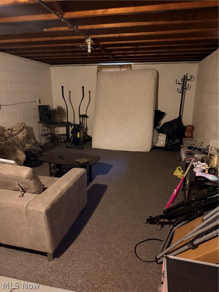 Basement with exposed ceiling joists, carpet, a sofa, exercise equipment, and stored belongings.