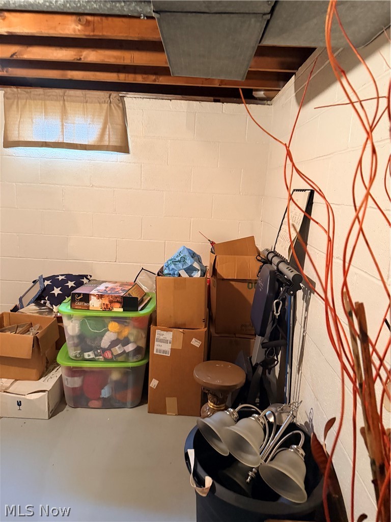 Unfinished basement storage area with exposed joists, stacked boxes, storage bins, and exercise equipment.