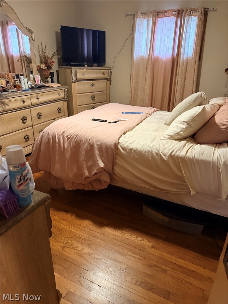 Bedroom with blush-pink bedding, matching wooden dressers, a television, and hardwood floors.