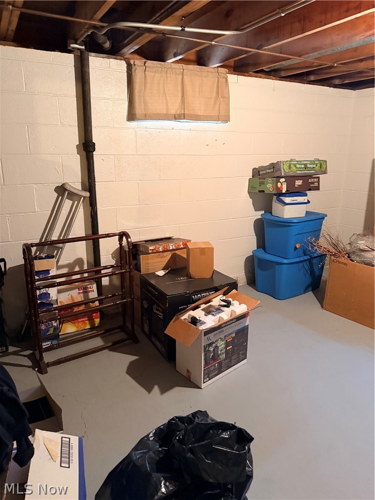 Basement storage area with exposed ceiling joists, concrete floor, boxes, and blue storage bins.