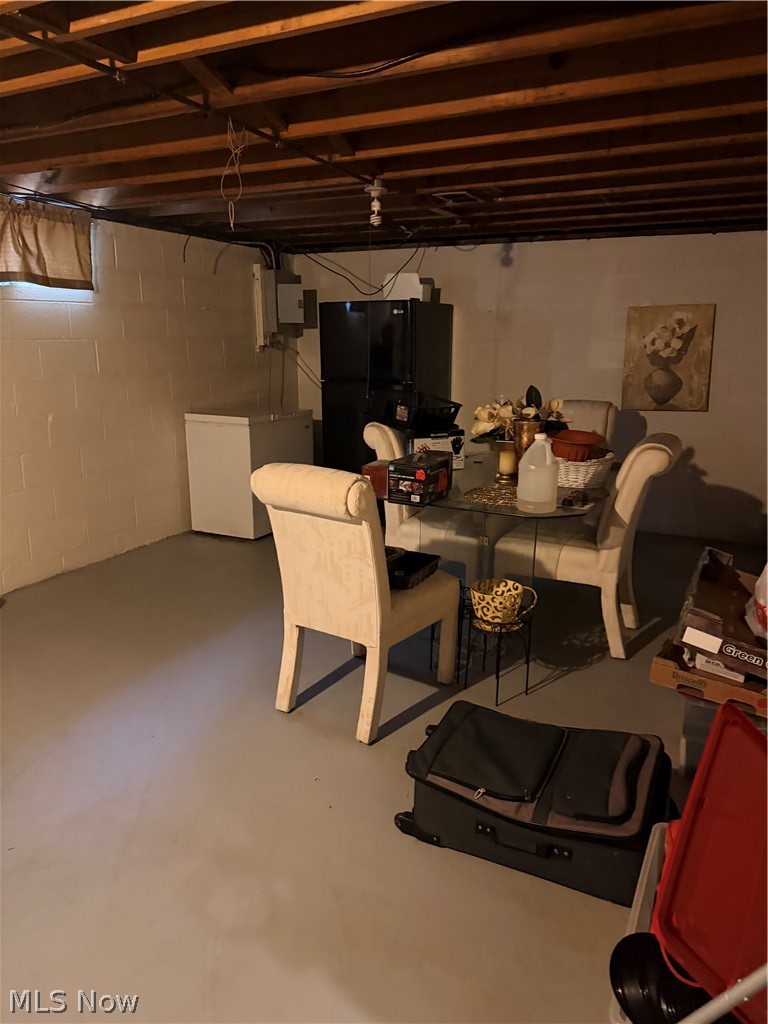 Unfinished basement with exposed ceiling joists, a dining table, and household storage.