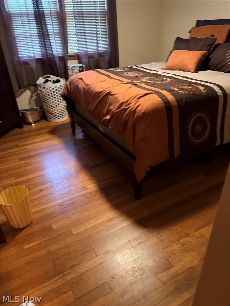 Bedroom with orange and brown patterned bedding, hardwood floors, and windows with blinds.