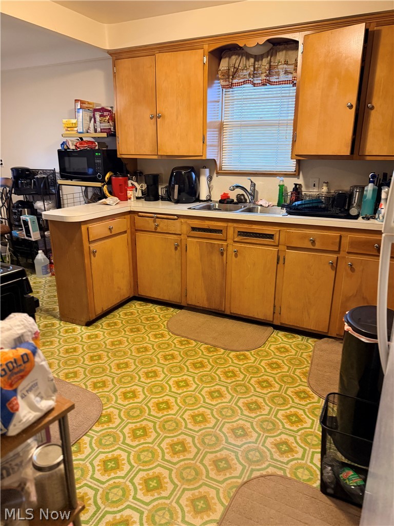 Kitchen with honey-colored wood cabinets, a double-basin sink, and a green-and-yellow patterned floor.