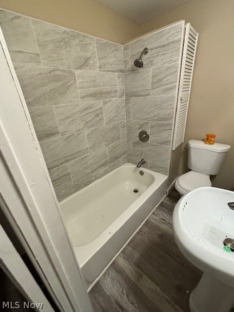 Bathroom with a gray tiled tub and shower, toilet, and pedestal sink.