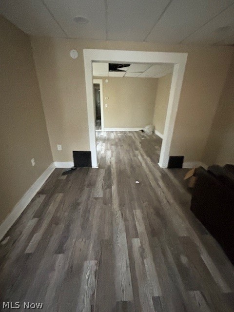 Empty room with gray plank flooring, beige walls, and missing ceiling tiles.