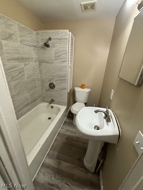 Bathroom with a gray tiled tub surround, pedestal sink, and gray flooring.