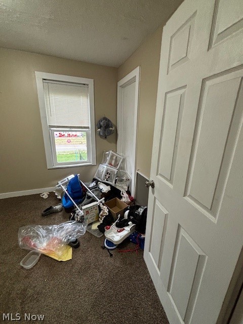 Small carpeted room with a window, open door, and belongings scattered across the floor.