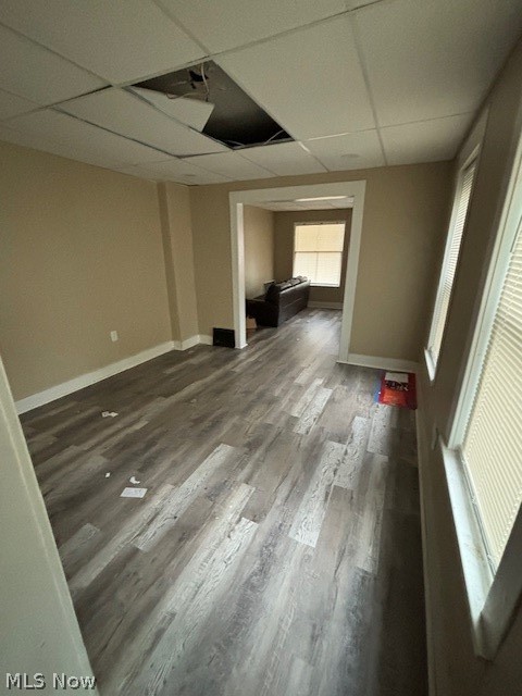 Long room with gray plank flooring, tall windows, and a damaged ceiling tile.
