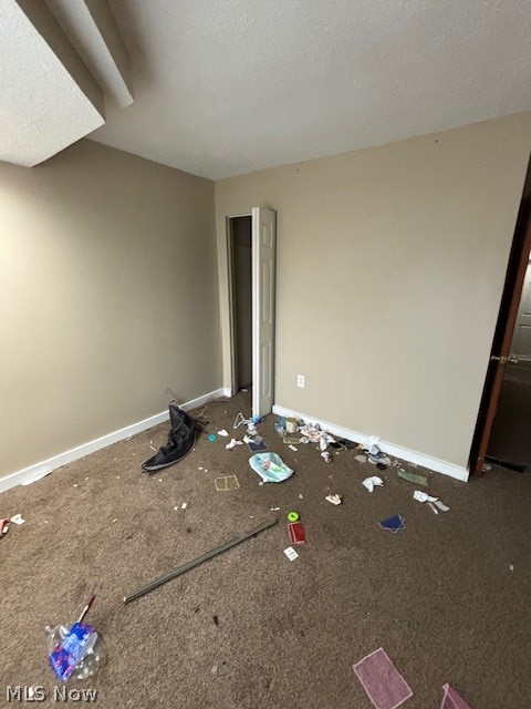 Empty carpeted room with beige walls, scattered debris, and an open doorway.