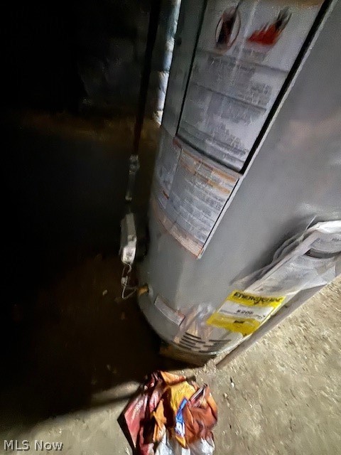 Water heater in a dim utility area, with warning labels and fabric on the floor.