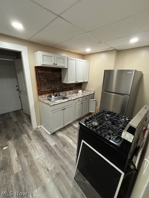 Kitchen with white cabinets, a dark wood backsplash, stainless steel refrigerator, and black range.