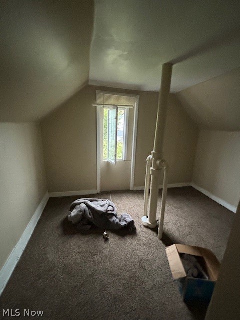 Carpeted upper-floor room with a sloped ceiling, narrow window, and exposed pipes.
