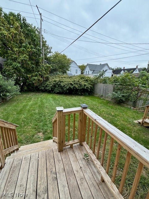 Wooden deck overlooking a fenced grassy backyard bordered by shrubs and neighboring homes.