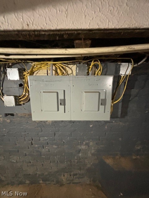 Basement electrical panels mounted on an exposed brick wall beneath utility wiring.
