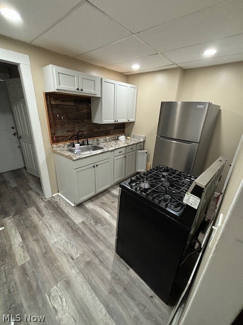 Kitchen with white cabinets, a dark wood backsplash, stainless refrigerator, and black gas range.