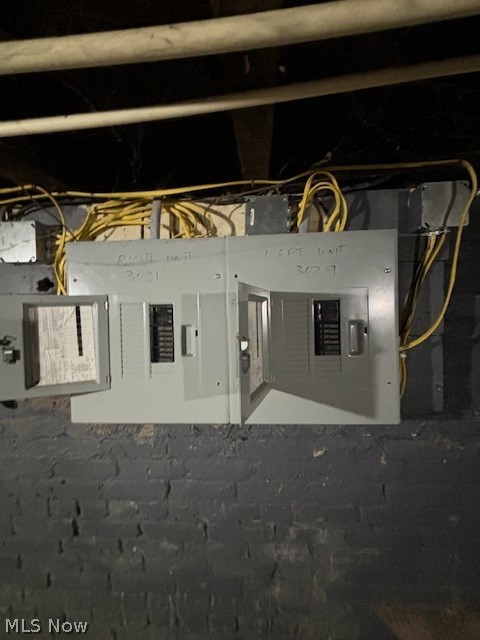Two electrical breaker panels mounted on an exposed brick basement wall, with visible wiring.
