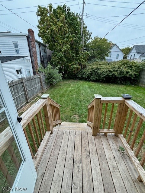 Wooden back deck and stairs overlooking a fenced grassy backyard with mature trees.
