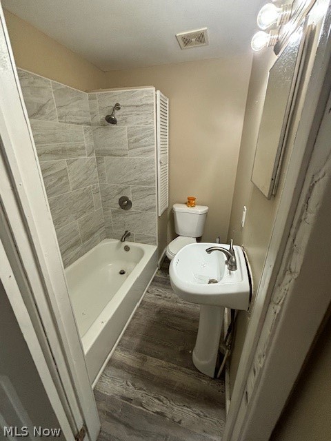Bathroom with a gray tiled tub and shower, pedestal sink, and wood-look flooring.