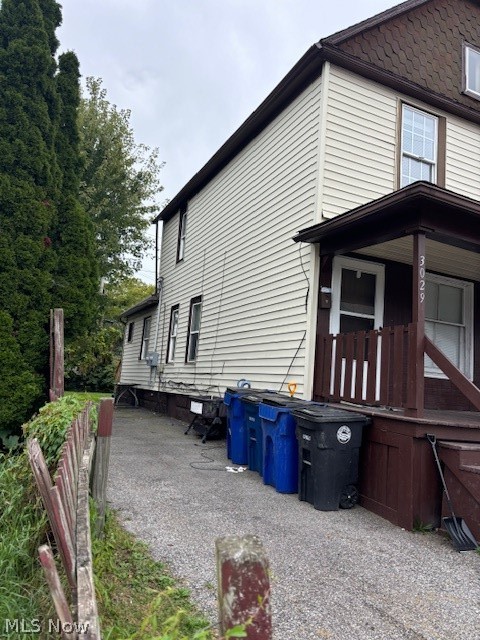 Two-story house with light siding, a covered porch, and bins along the driveway.