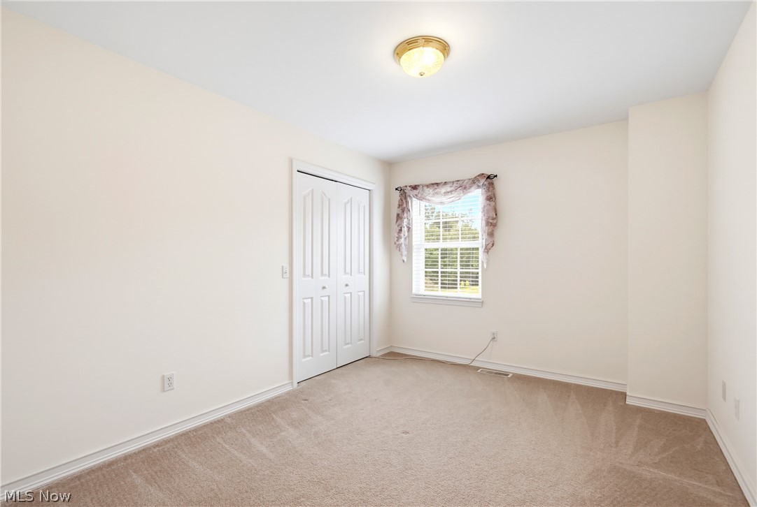 Empty carpeted bedroom with a double-door closet and a window with patterned curtains.