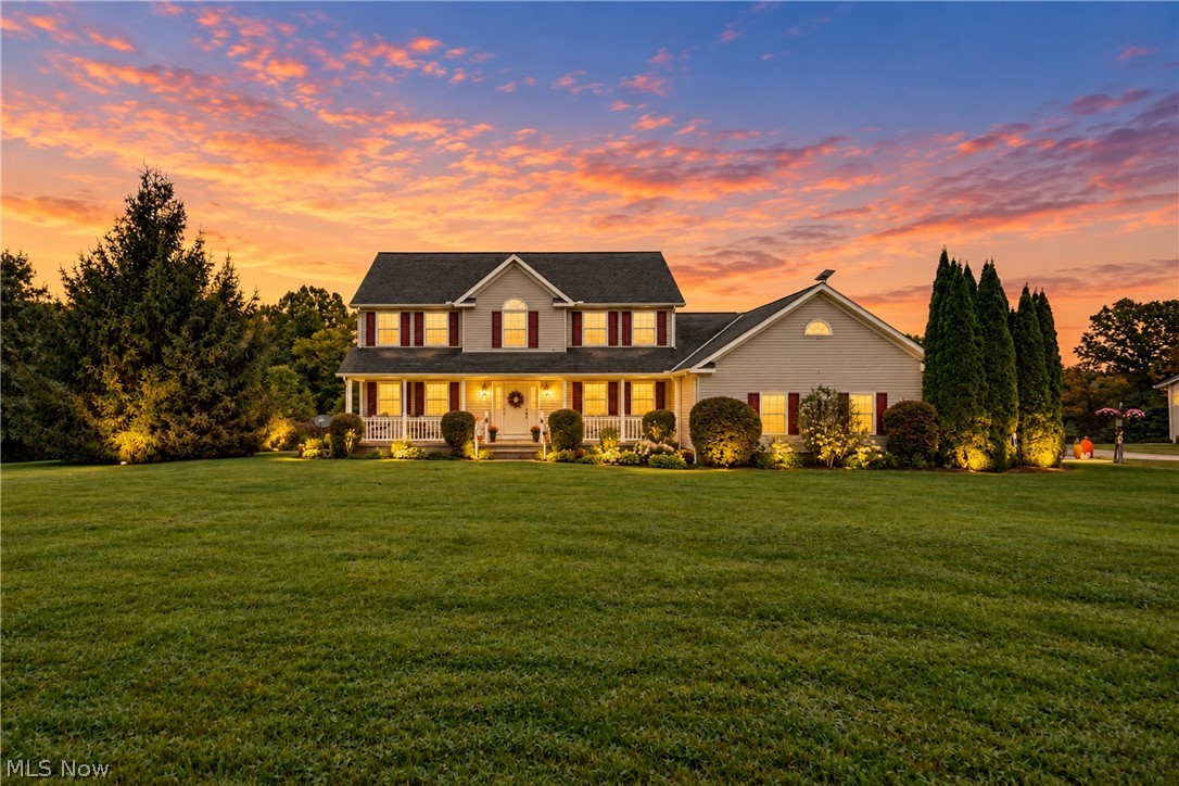 Two-story home with a covered porch and broad lawn beneath a colorful sunset sky.