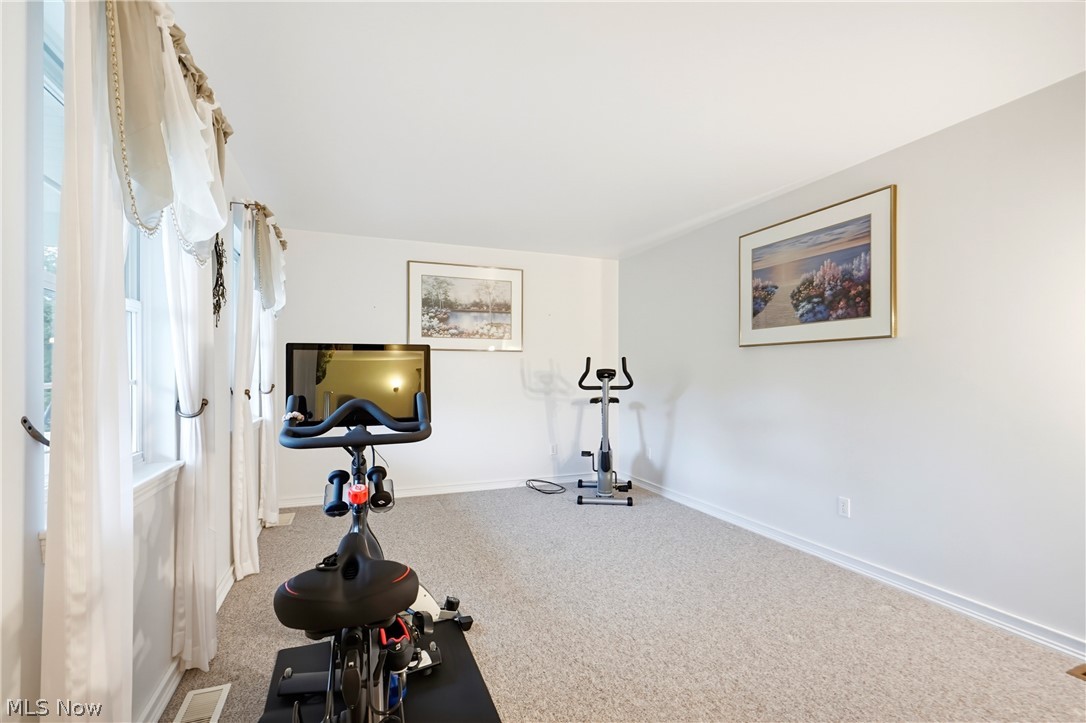Exercise room with a stationary bike, elliptical trainer, and tall curtained windows.