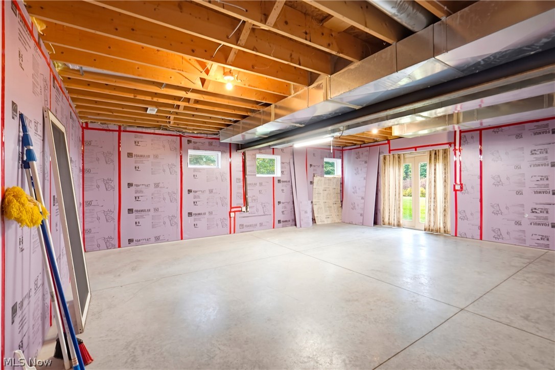 Unfinished room with pink wall insulation, exposed ceiling joists, large HVAC ducts, and a concrete floor.