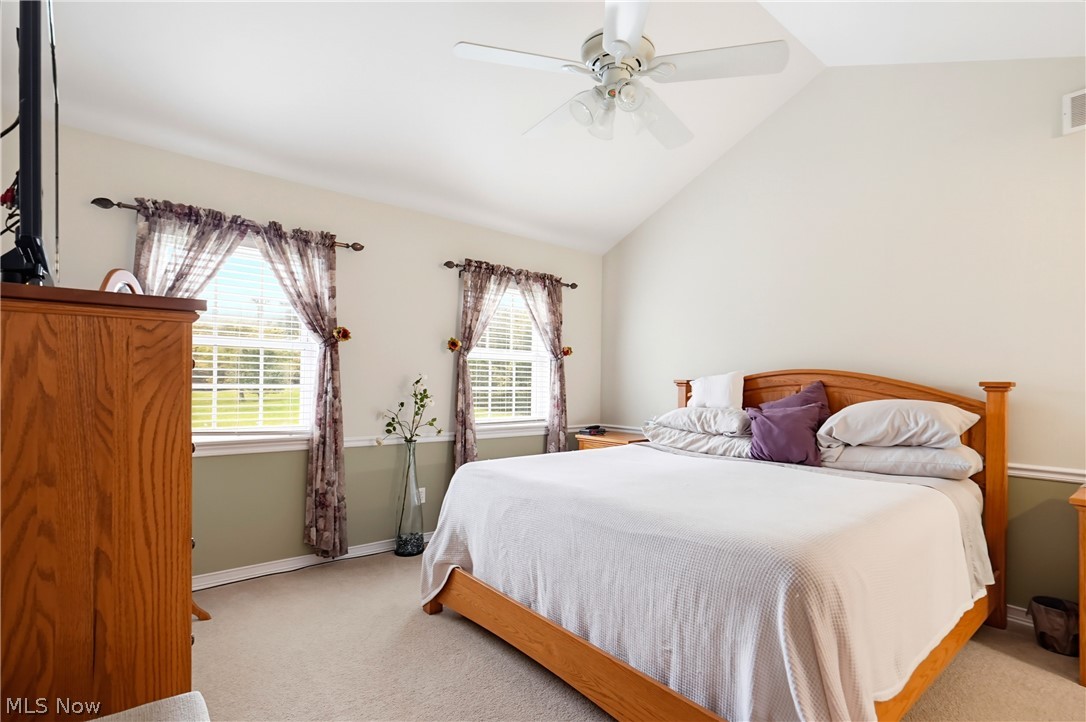 Bedroom with a wooden bed, purple accent pillows, and two curtained windows.