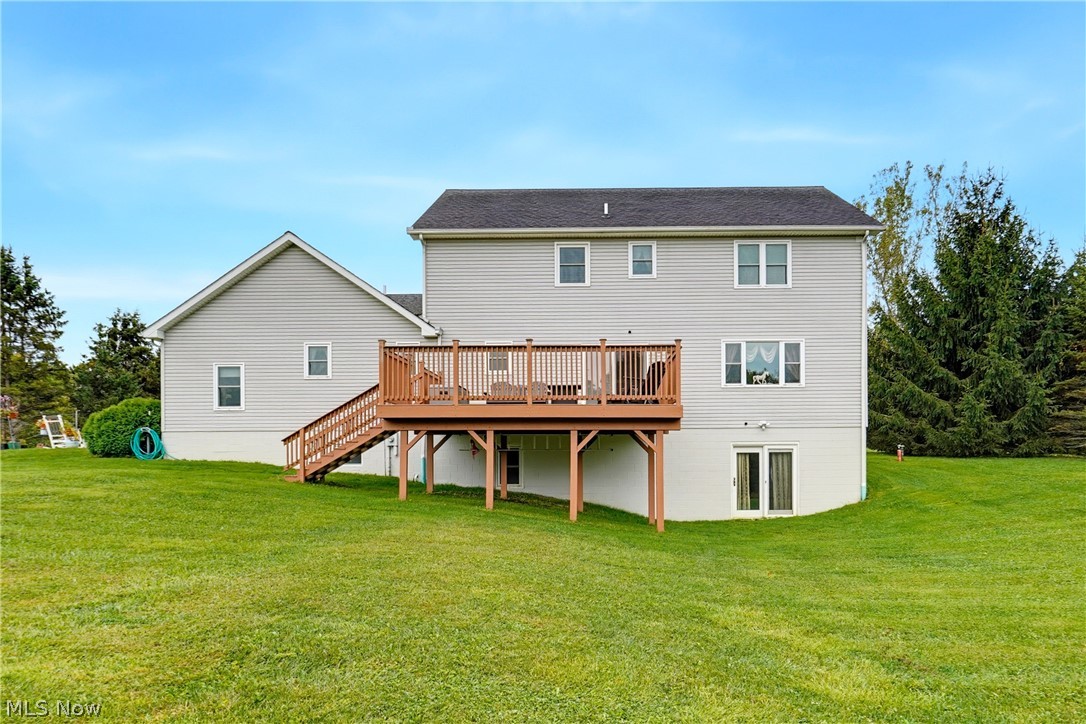 Rear of a gray two-story house with a raised wooden deck and broad lawn.