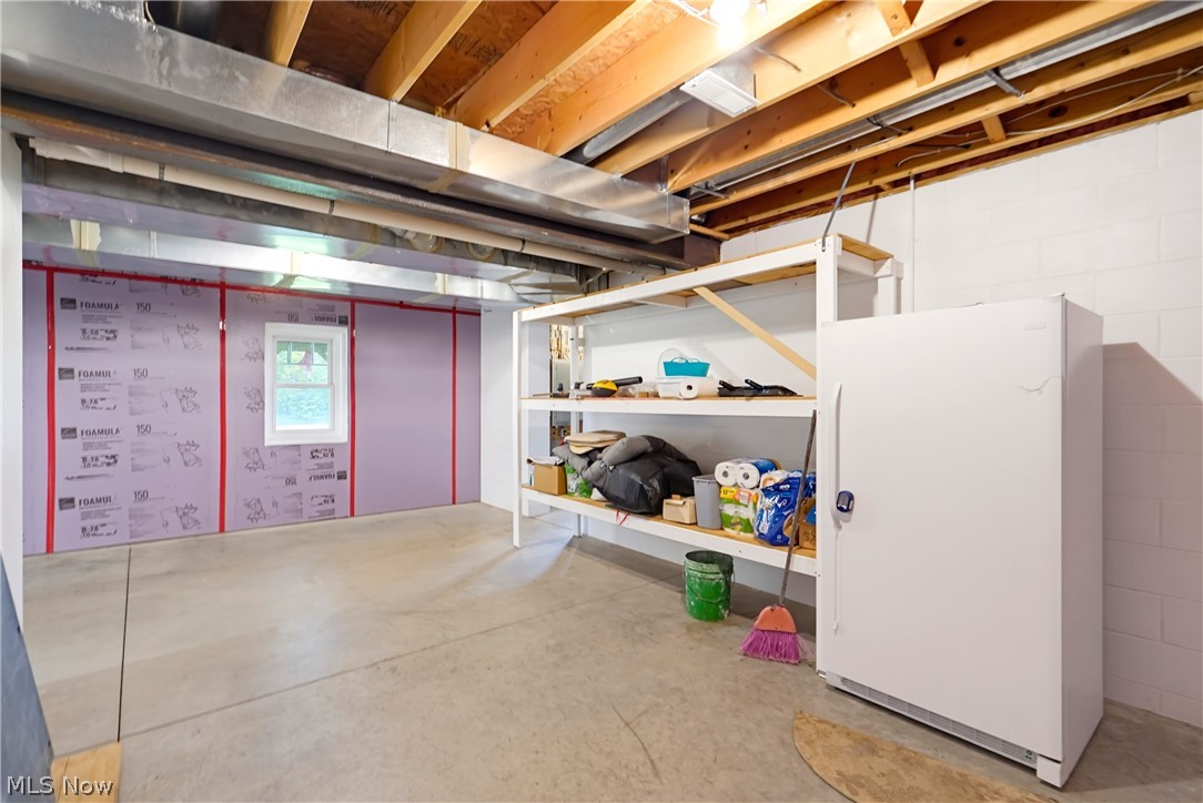 Basement storage area with exposed ceiling joists, white shelving, and a large freezer.