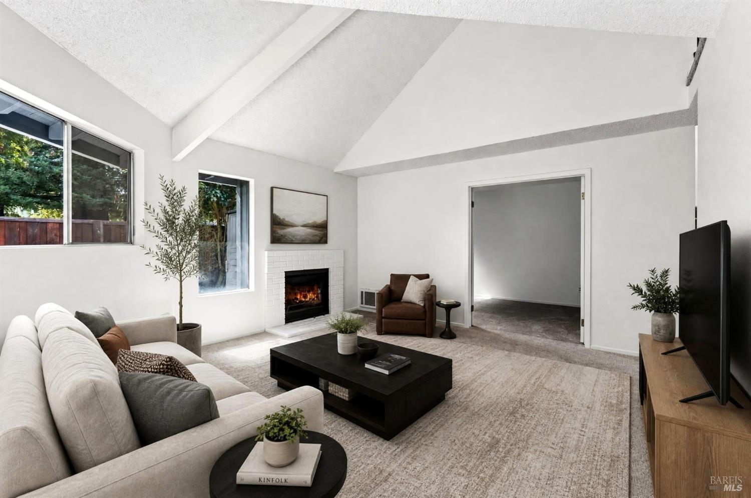 Furnished living room with a vaulted ceiling, lit fireplace, and large windows.
