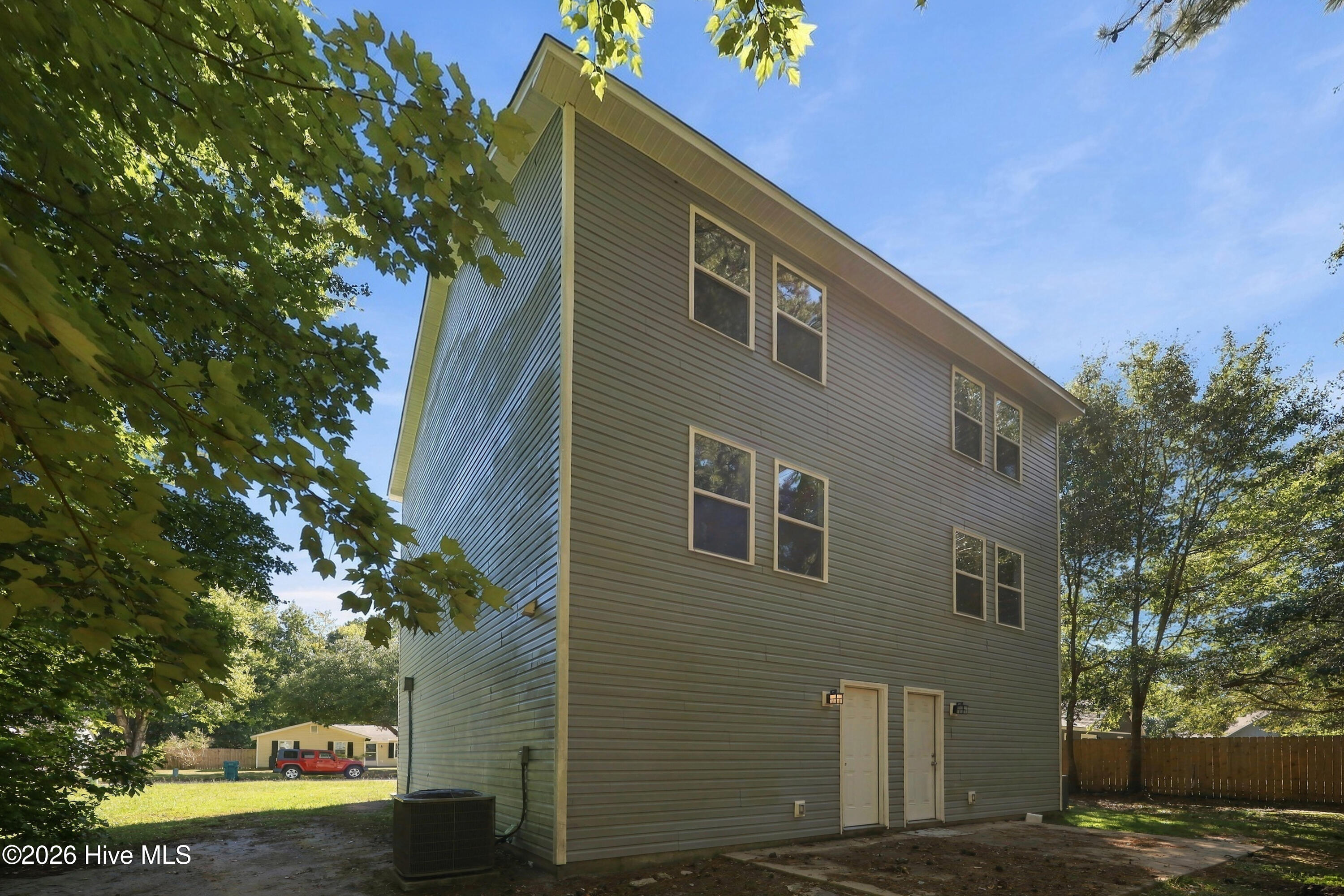 Tall gray-sided home with multiple windows and two ground-level doors, viewed from the side.
