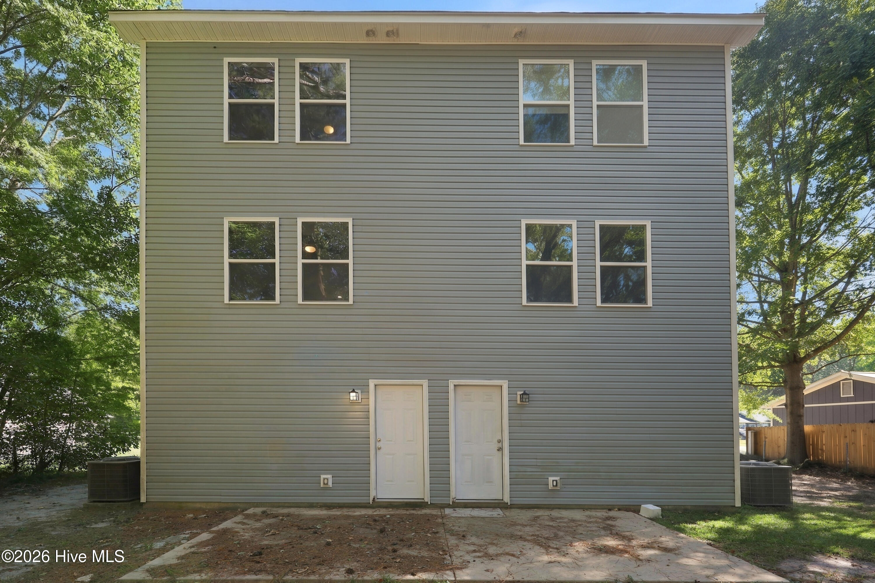Gray two-story home with two ground-floor doors, multiple windows, and mature trees nearby.