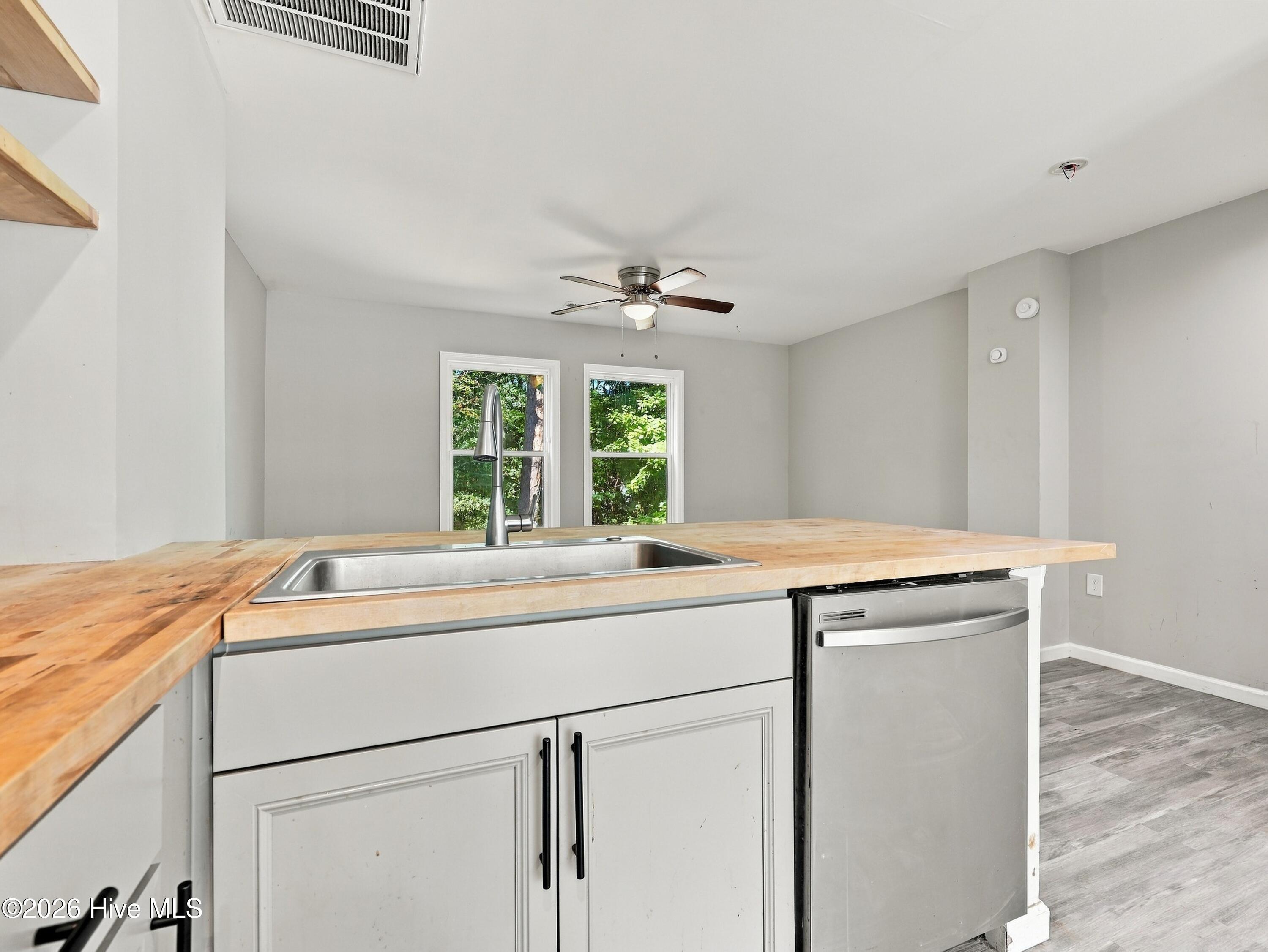 Vacant kitchen with butcher-block counters, a stainless sink, and windows overlooking trees.