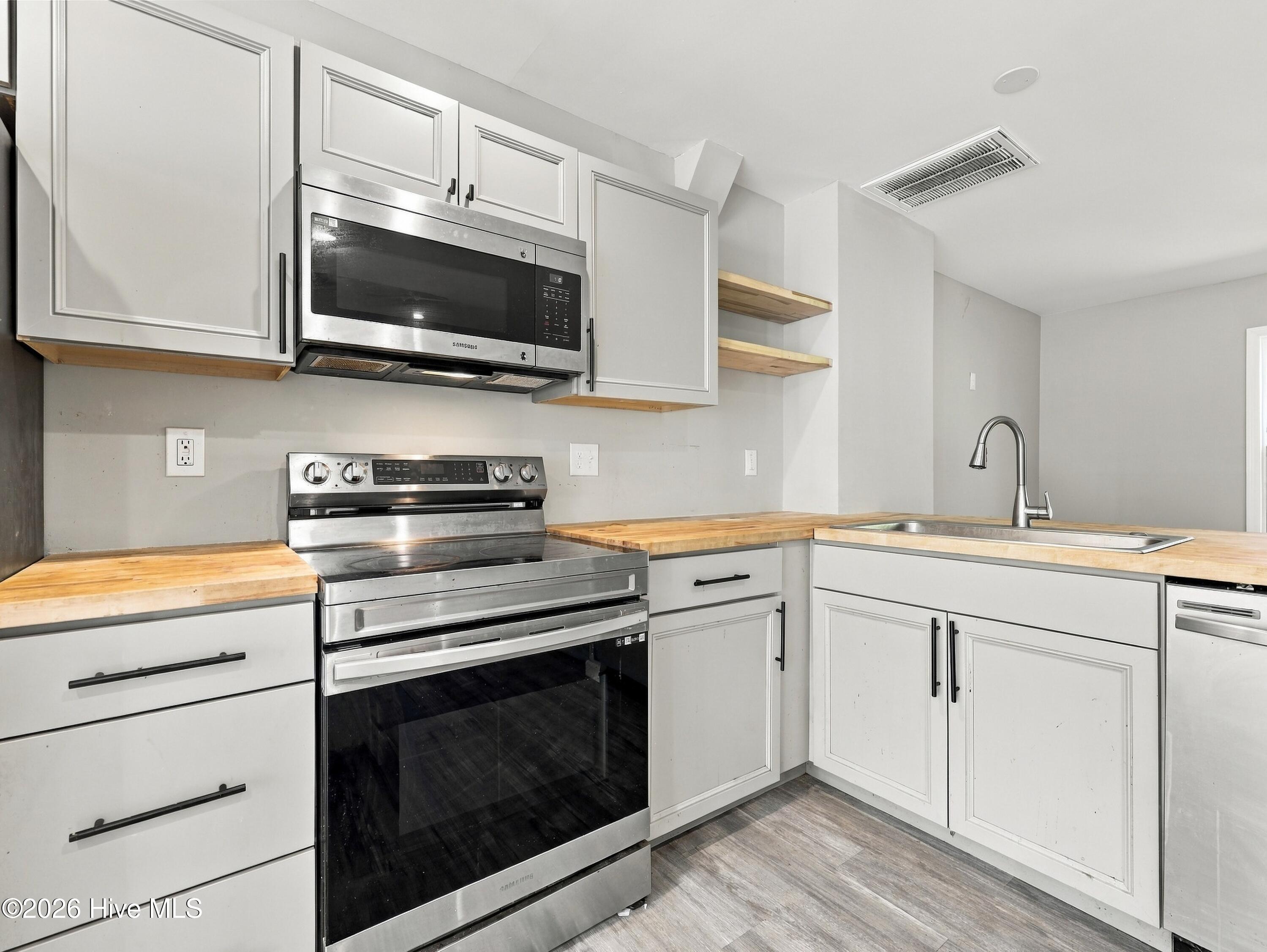 Kitchen with white cabinets, butcher-block counters, stainless steel appliances, and open wood shelves.