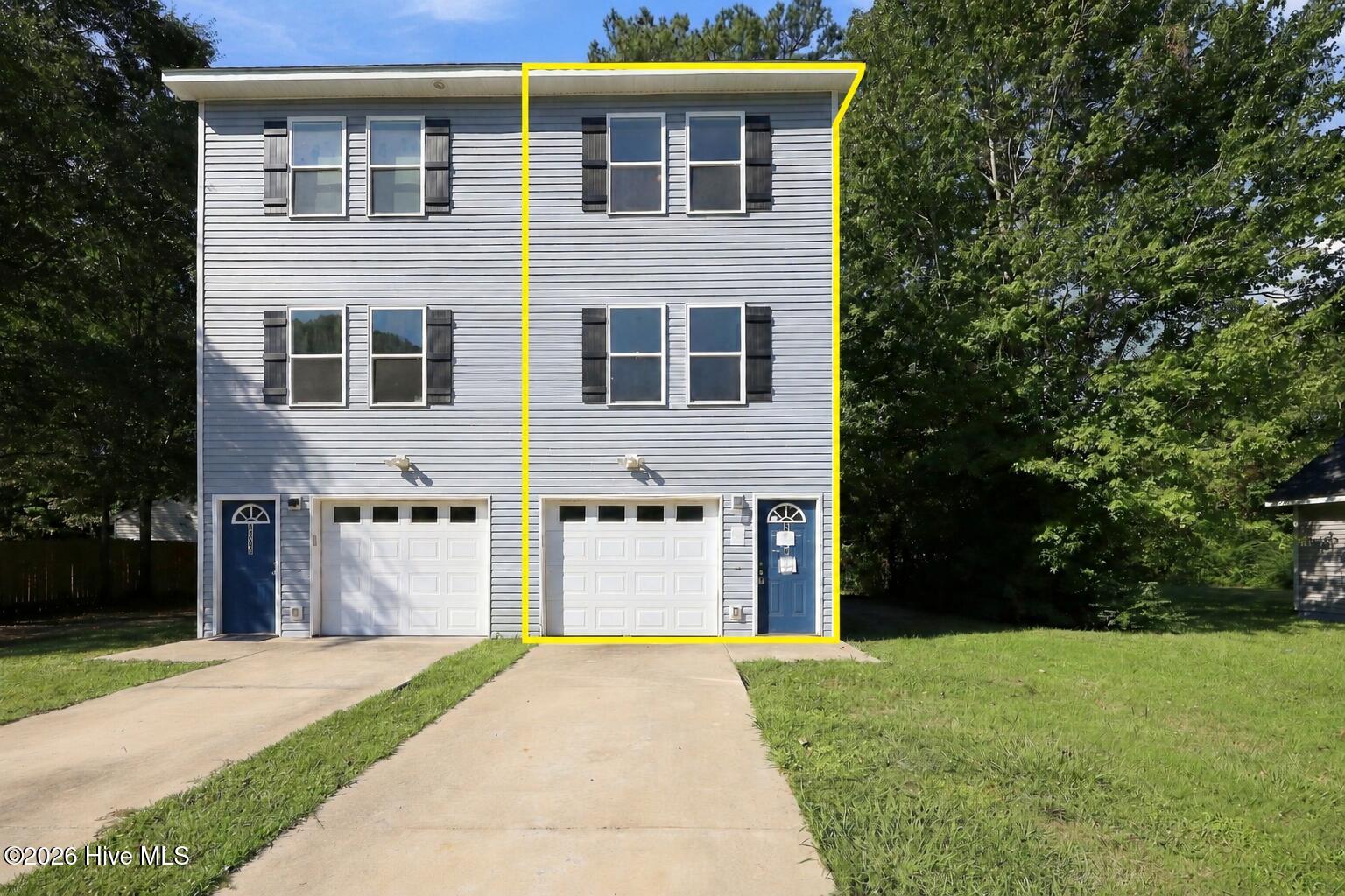 Highlighted unit in a gray two-story duplex with a blue entry door and attached garage.