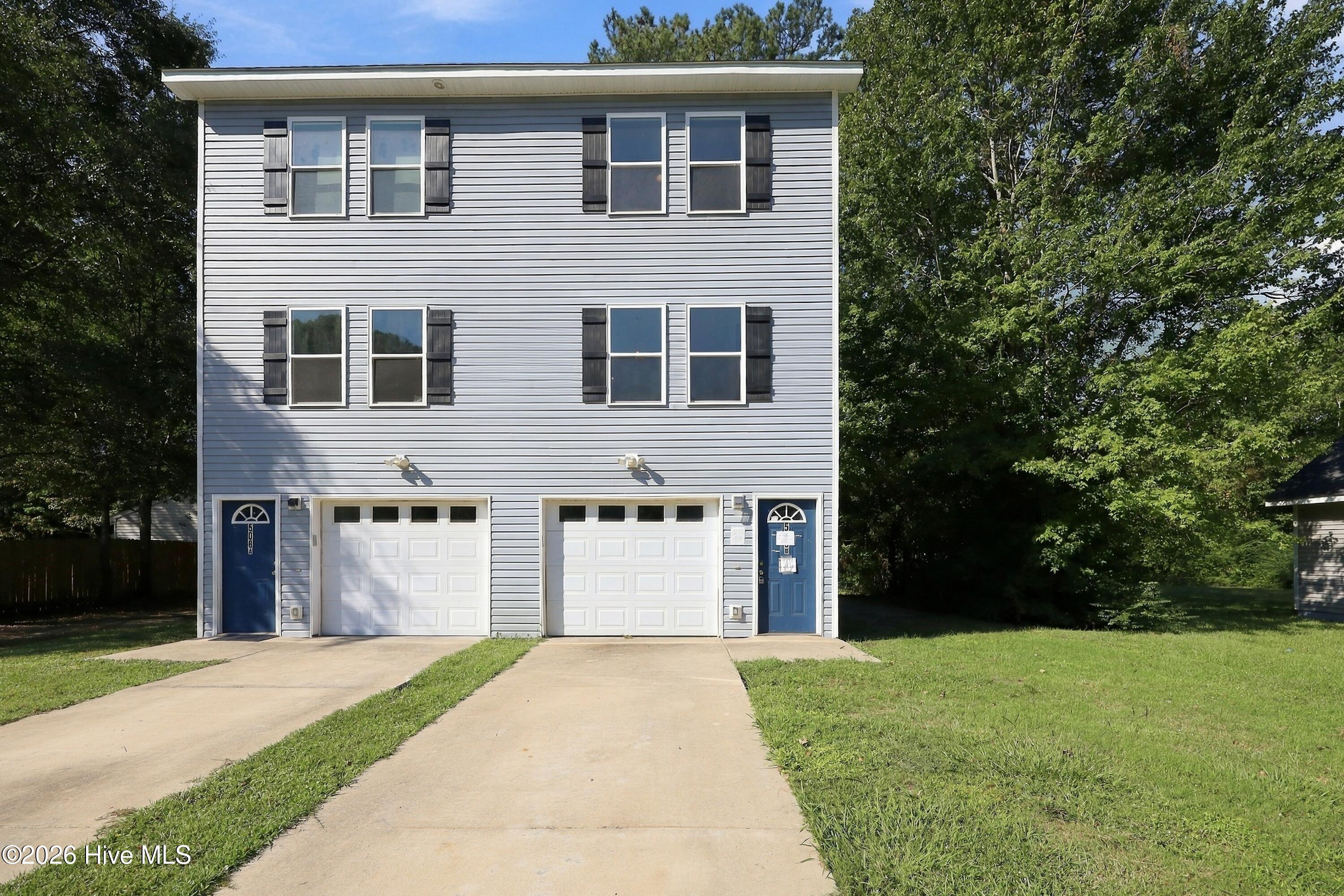 Two-story gray duplex with blue entry doors, white garage doors, and separate driveways.