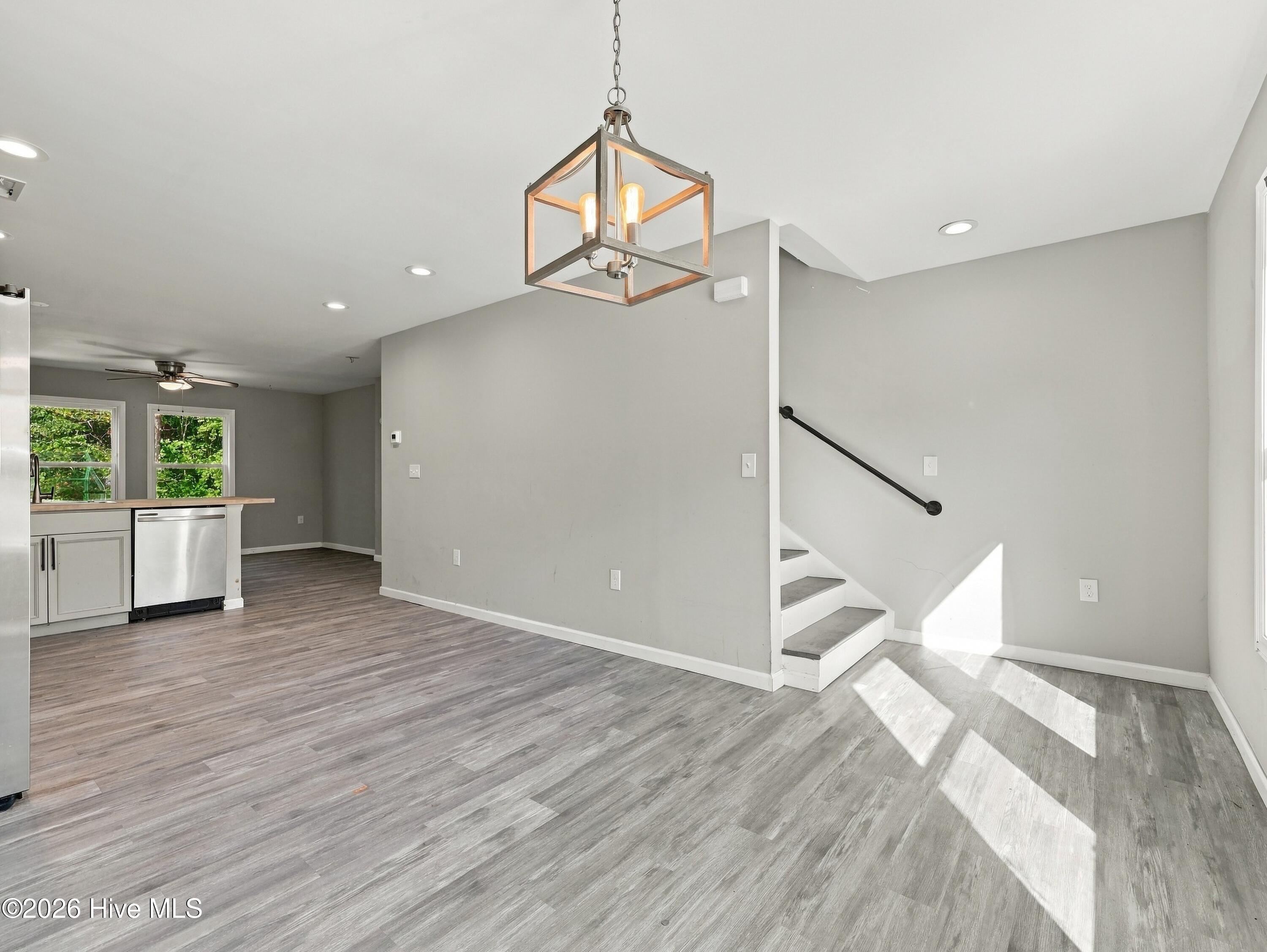 Open-plan living area with gray plank flooring, a staircase, and a kitchen peninsula.
