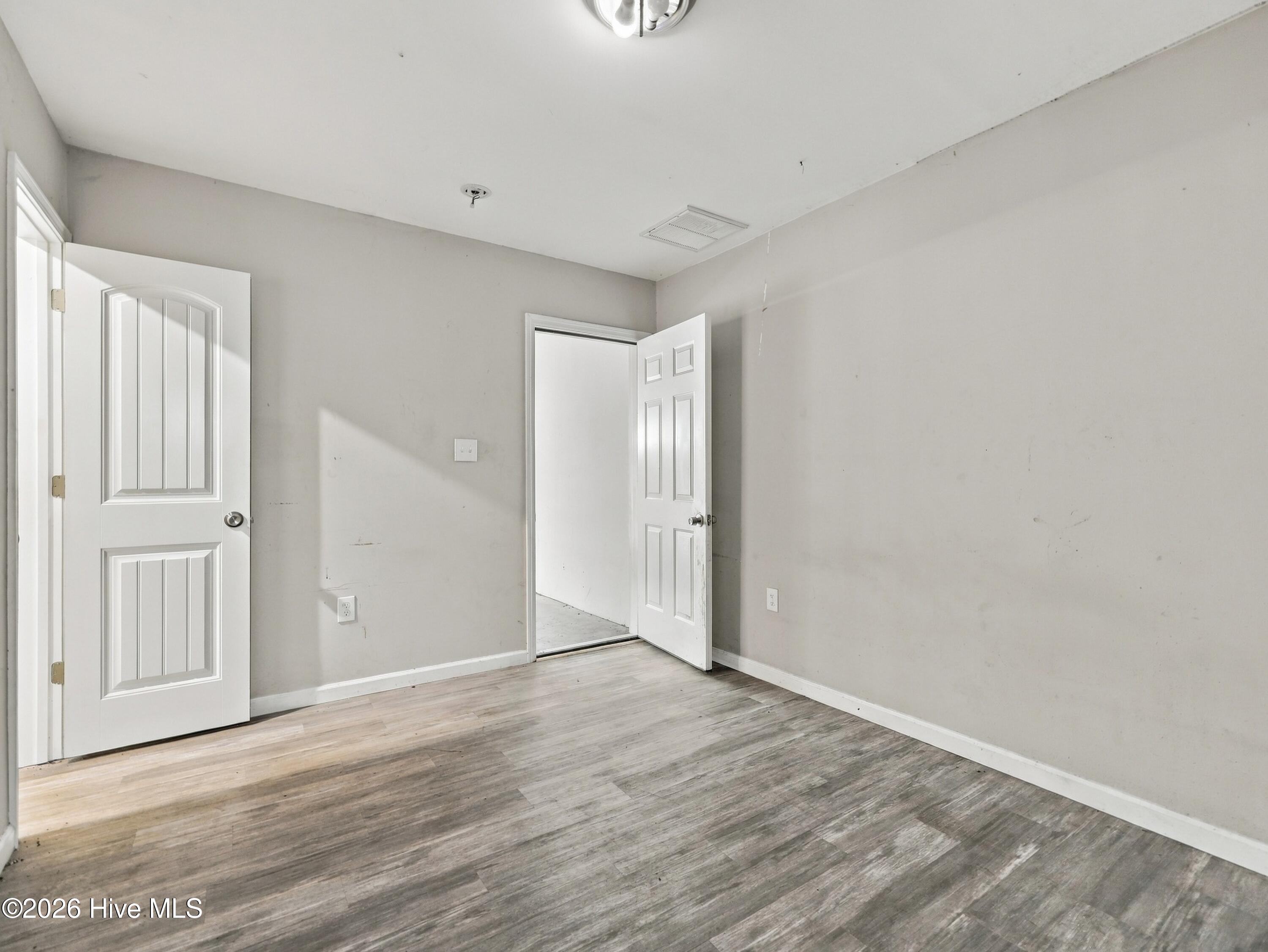Empty room with gray-brown plank flooring, gray walls, and two open white doors.