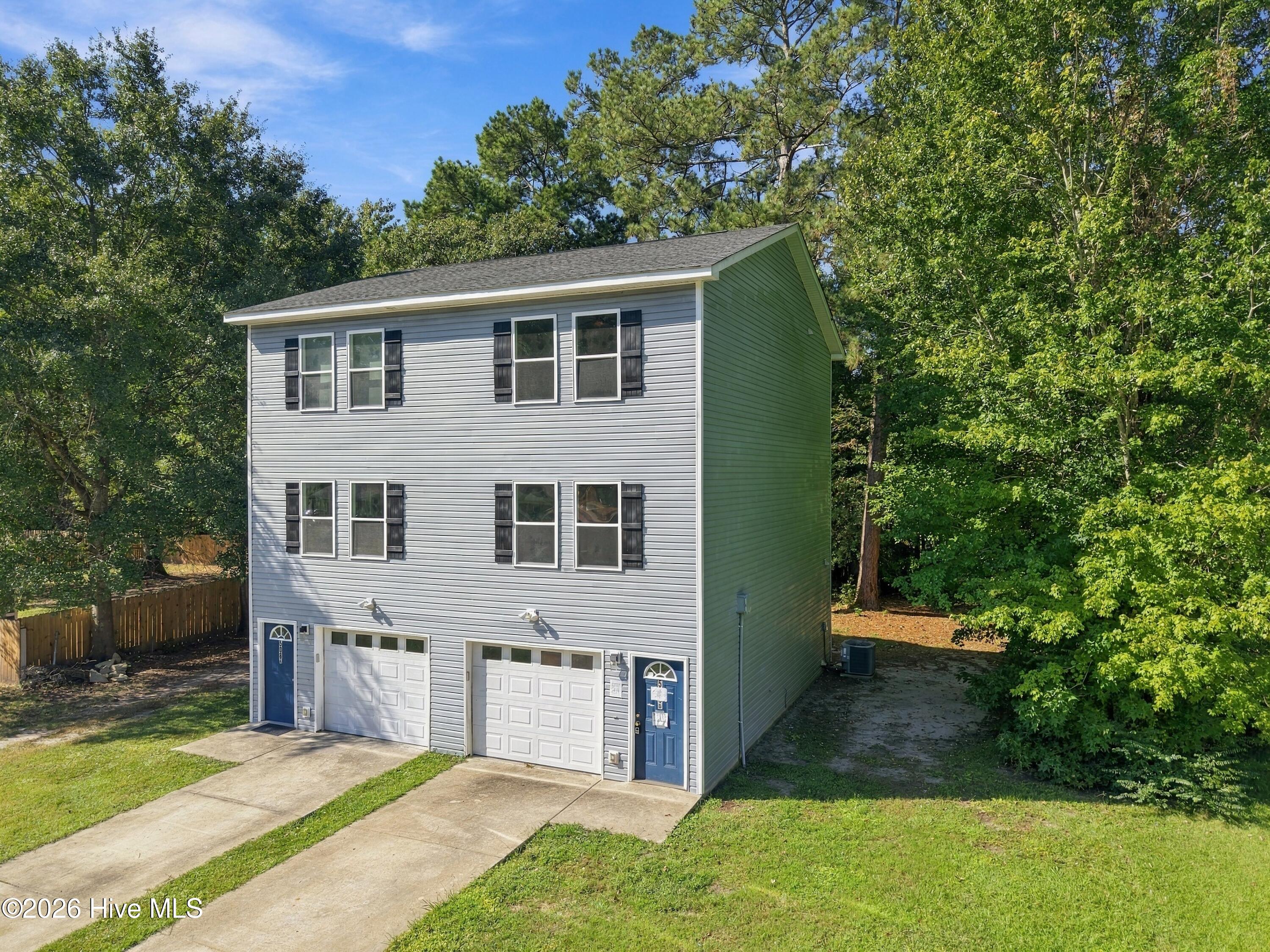 Gray two-story duplex with two garages and blue entry doors, set among mature trees.