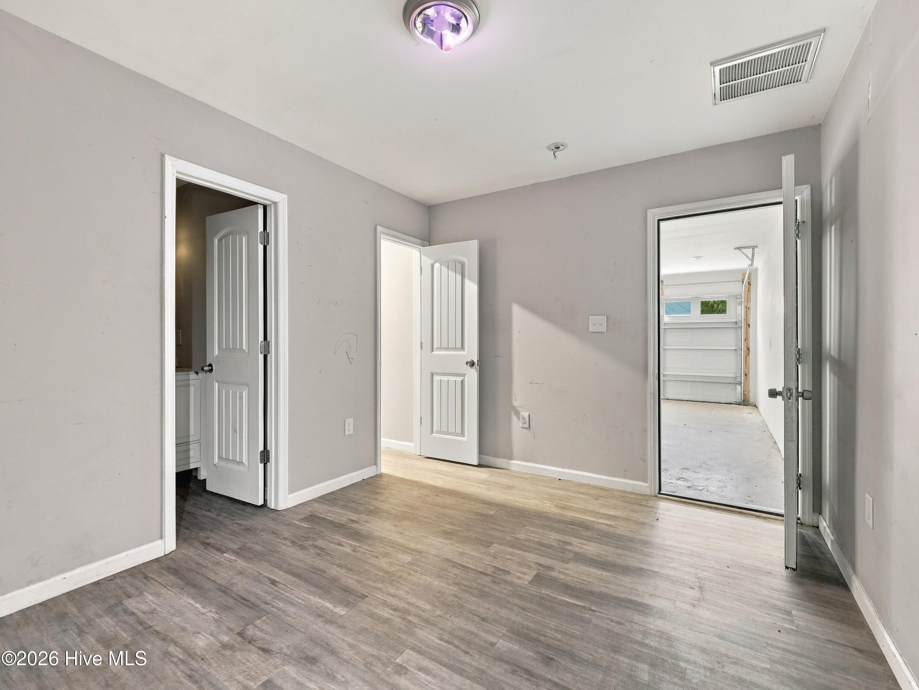 Empty room with gray walls and wood-look flooring, opening to a bathroom and garage.