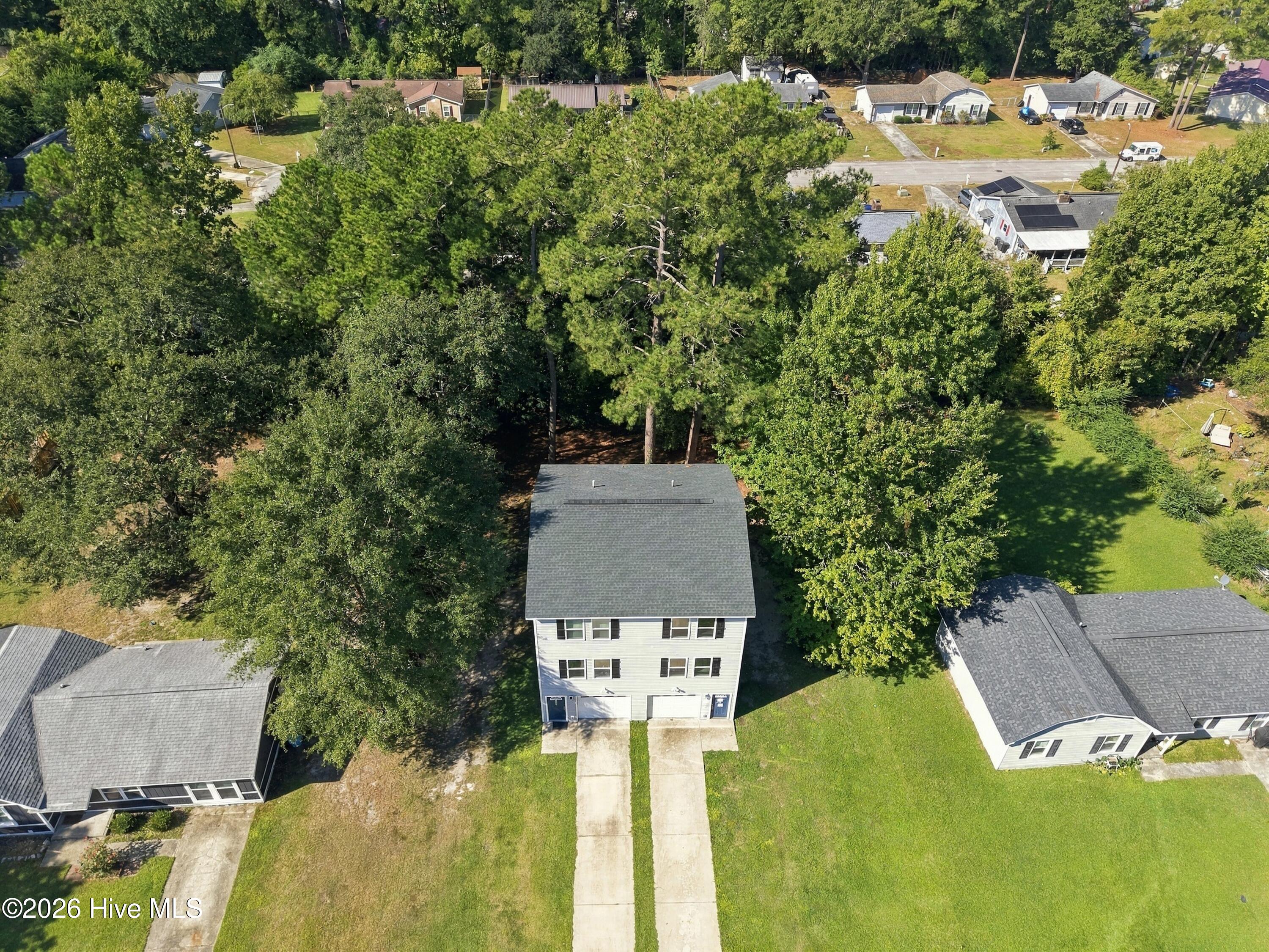 Aerial view of a two-story home bordered by mature trees, with two driveways and a broad front lawn.