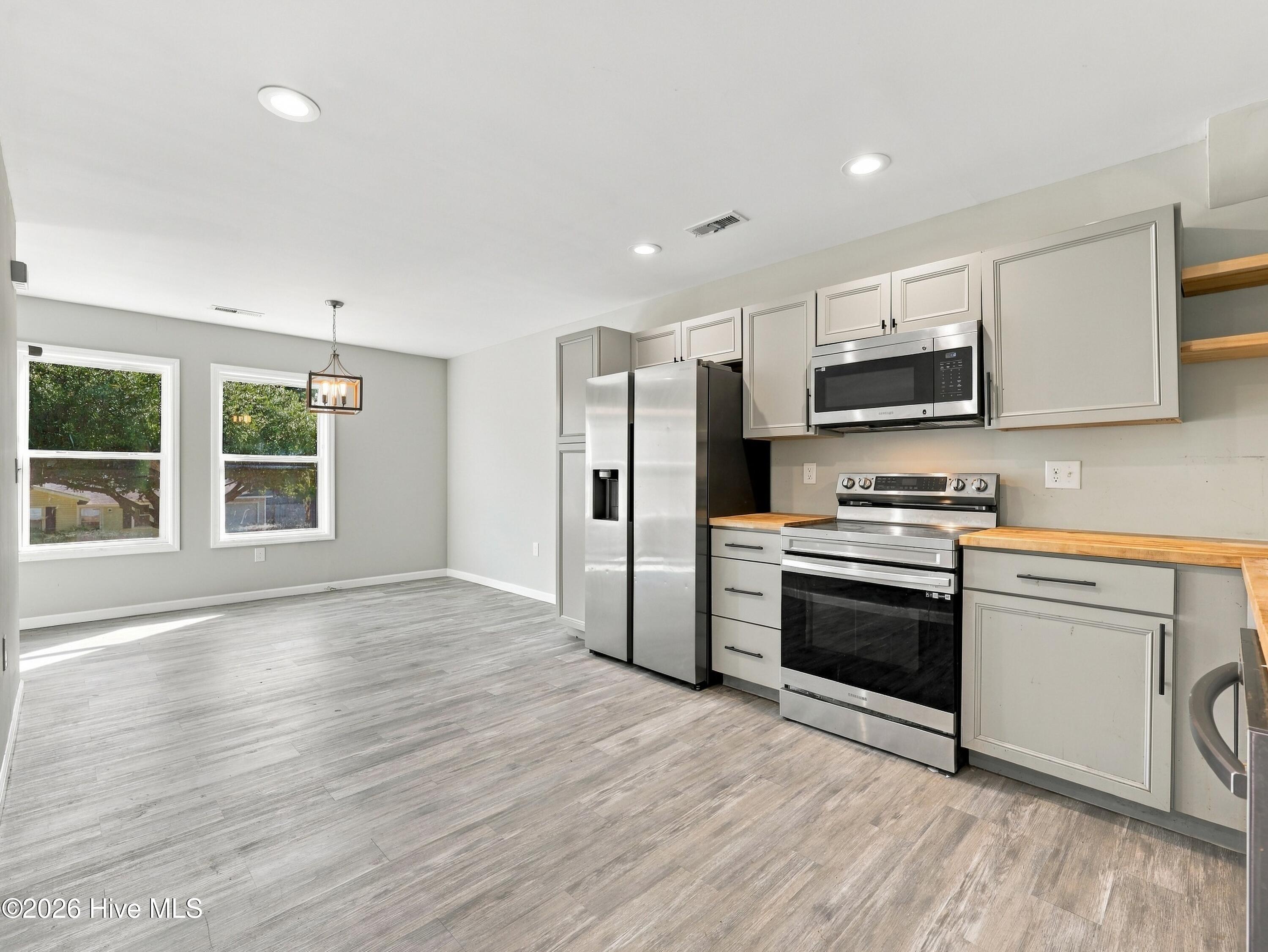 Kitchen with stainless steel appliances, gray cabinets, wood countertops, and an adjoining dining area.